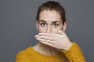 portrait of surprised young woman covering her mouth for silence