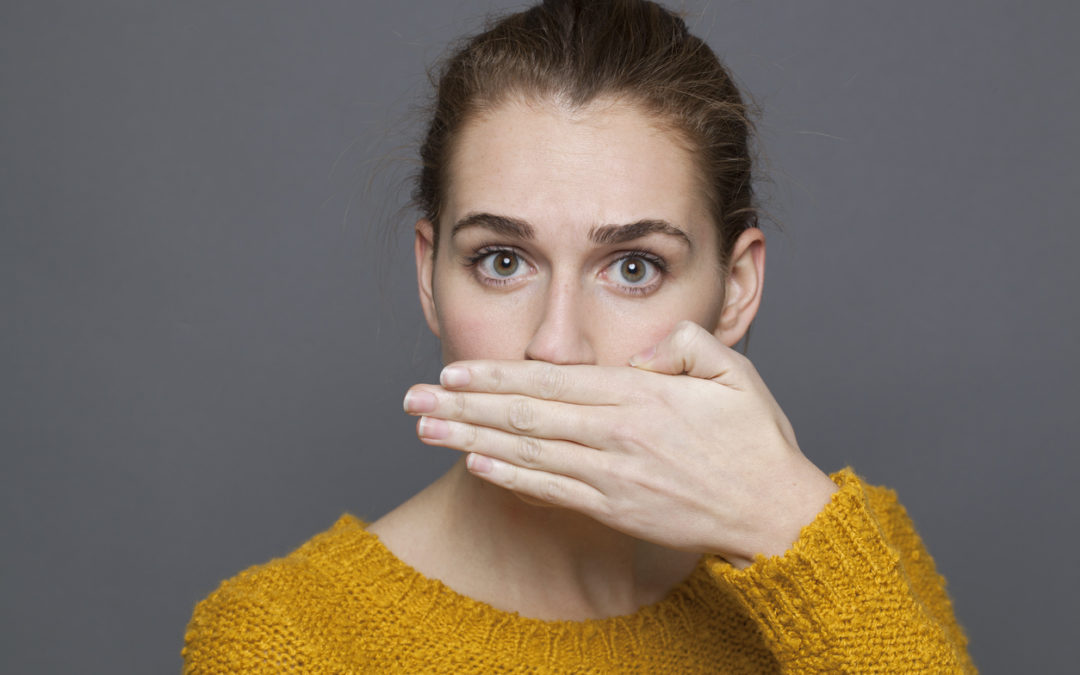 portrait of surprised young woman covering her mouth for silence