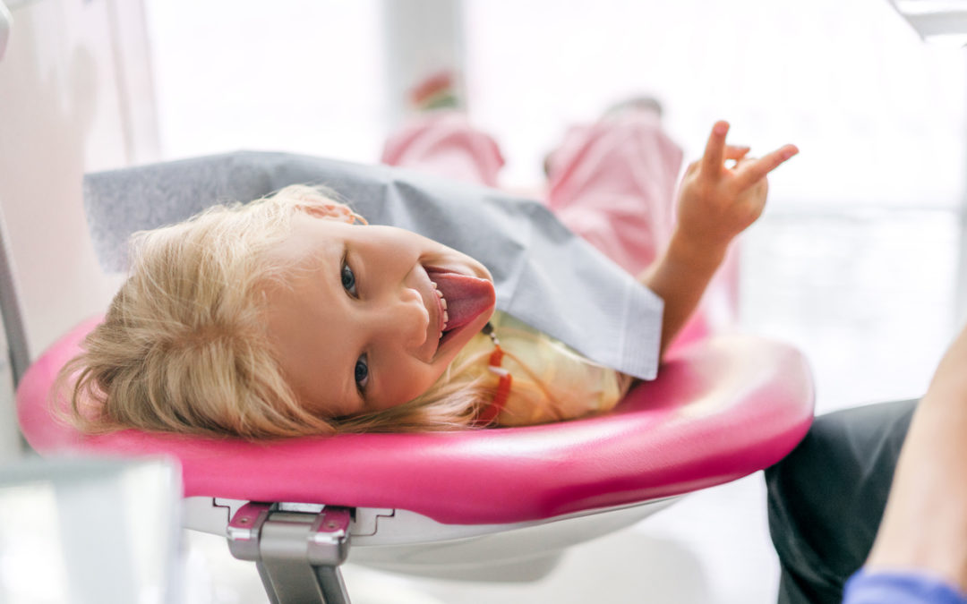 portrait of child sticking tongue out and showing peace sign at dentist office